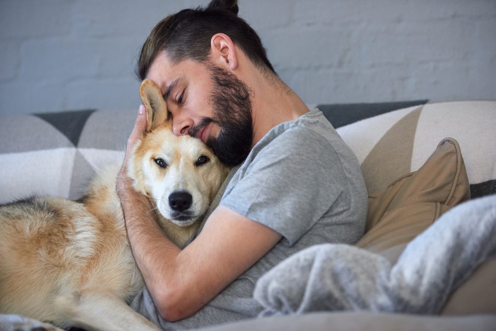 bearded man hugs dog while sitting on couch