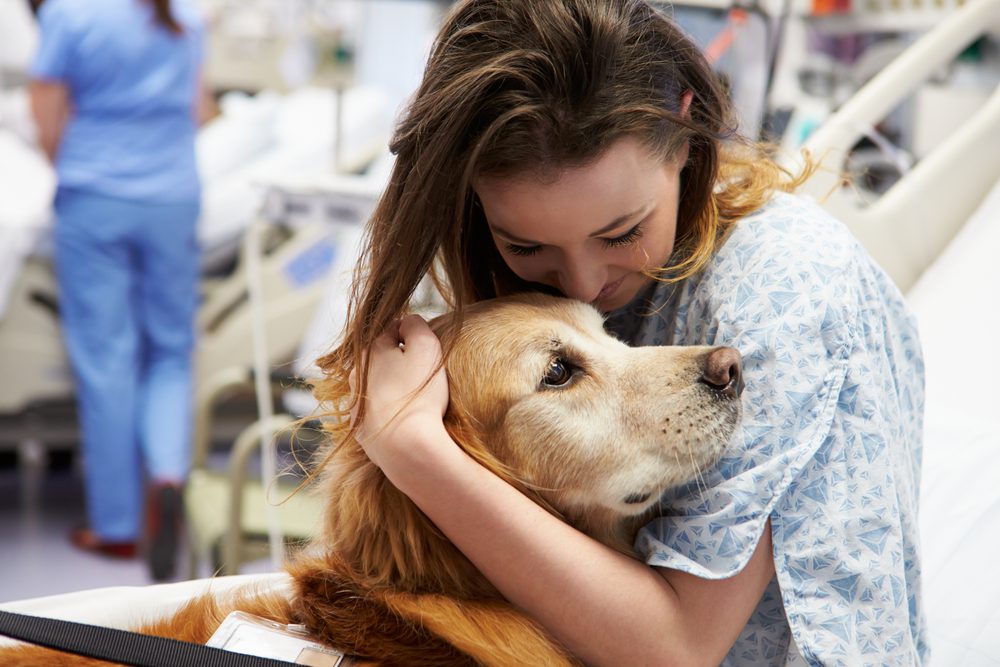 woman in hospital bed hugging dog