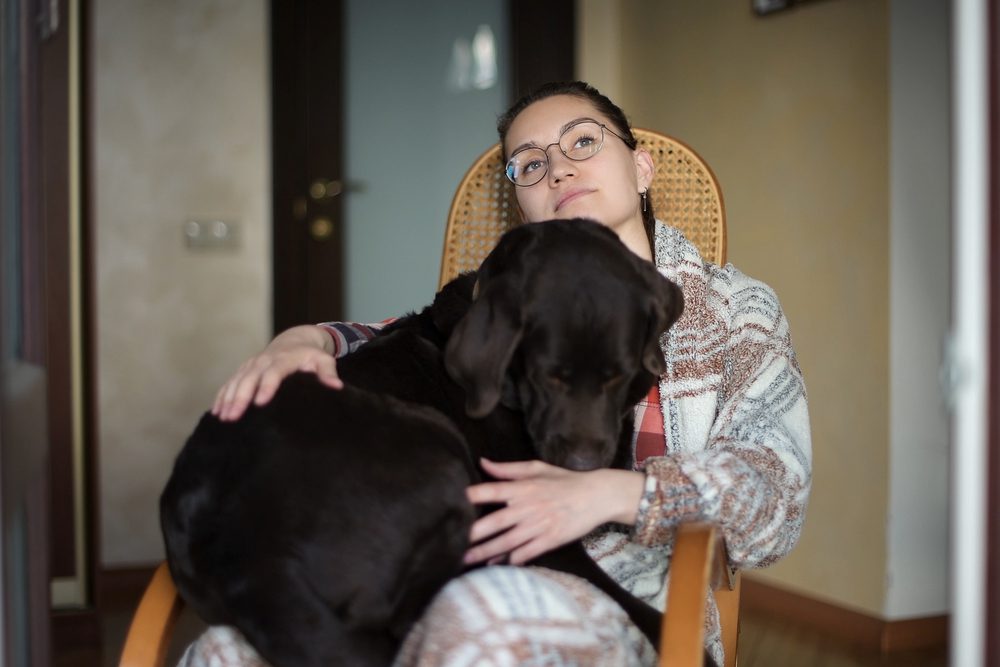 Black lab lays in woman’s lap sitting in rocking chair